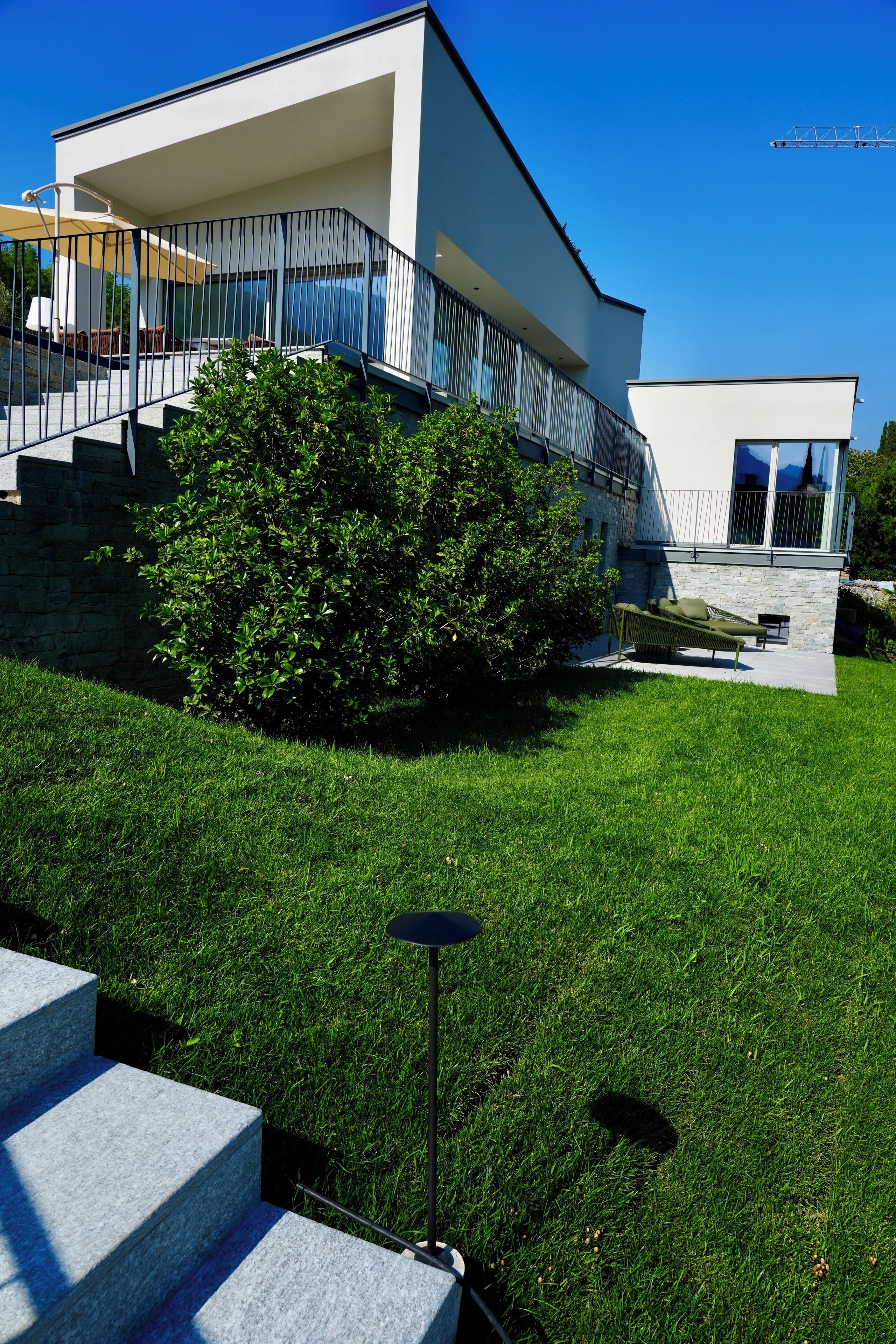 Une maison moderne à deux étages, dotée d’un balcon, d’une pelouse bien entretenue et d’un mur en pierre.