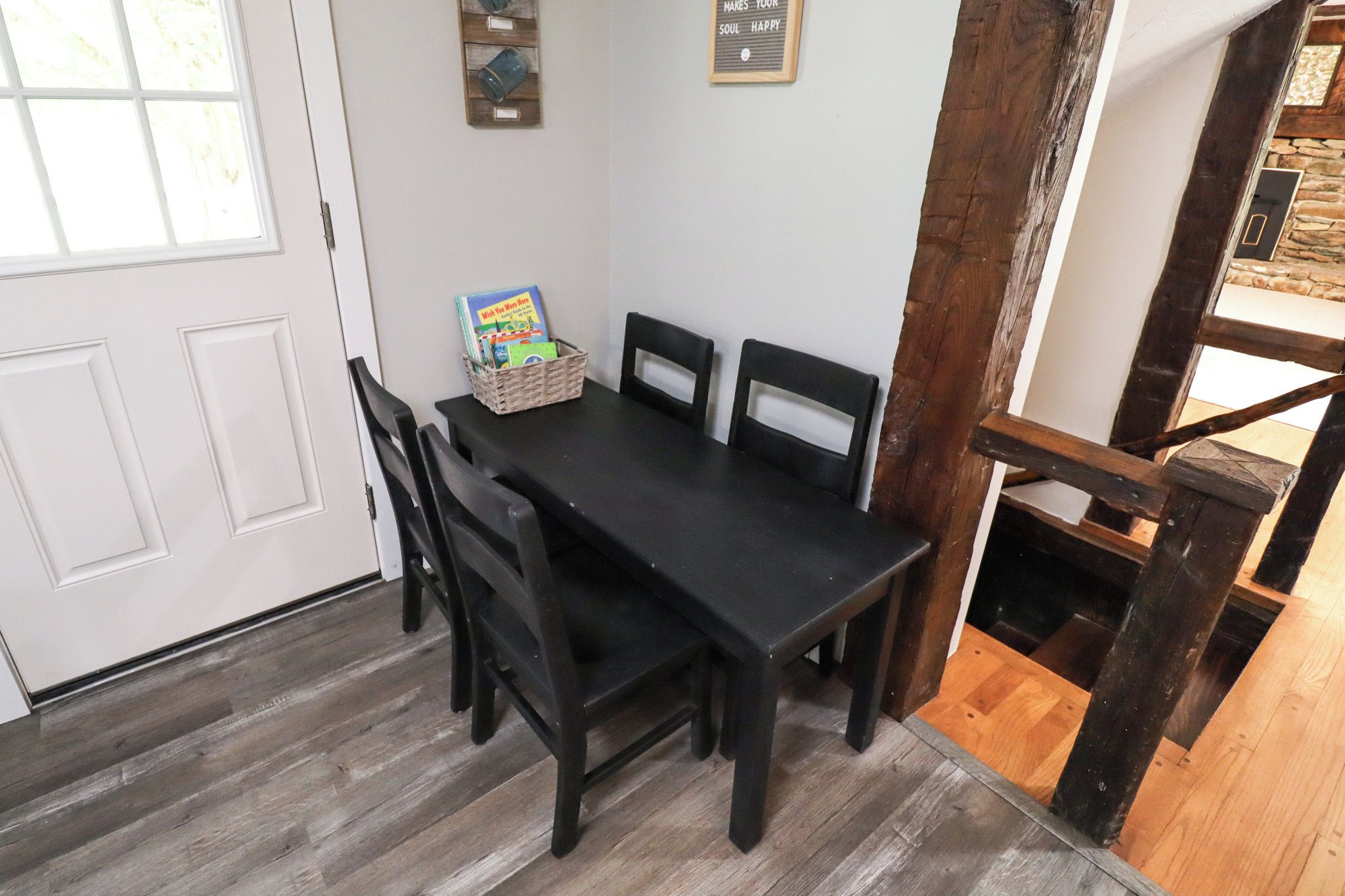 A dining area with a black table and chairs, a basket with books, and a light switch on the wall.