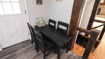A dining area with a black table and chairs, a basket with books, and a light switch on the wall.