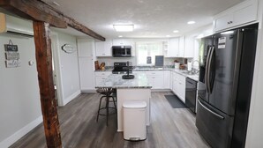 Una cocina moderna con armarios blancos, un refrigerador de acero inoxidable y una isla central con taburetes de bar.