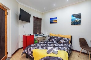 A bedroom with a bed, a desk, a television, and artwork on the walls. - Coastal stay in safest neighbourhood. (Cape Town)