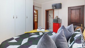Een slaapkamer met een bed, een kledingkast, een televisie en een kleine kitchenette.
