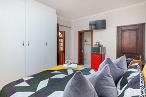 A bedroom with a bed, a wardrobe, a television, and a small kitchenette. - Coastal stay in safest neighbourhood. (Cape Town)