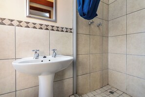 A bathroom with a white sink, two faucets, a mirror, and a shower area with tiled walls. - Coastal stay in safest neighbourhood. (Cape Town)