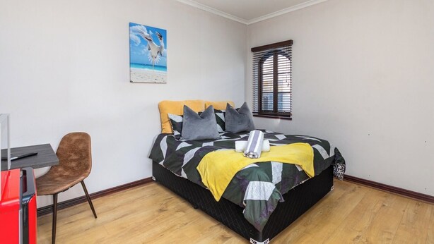 Een slaapkamer met een bed, een bureau, een stoel, een raam en een schilderij aan de muur.