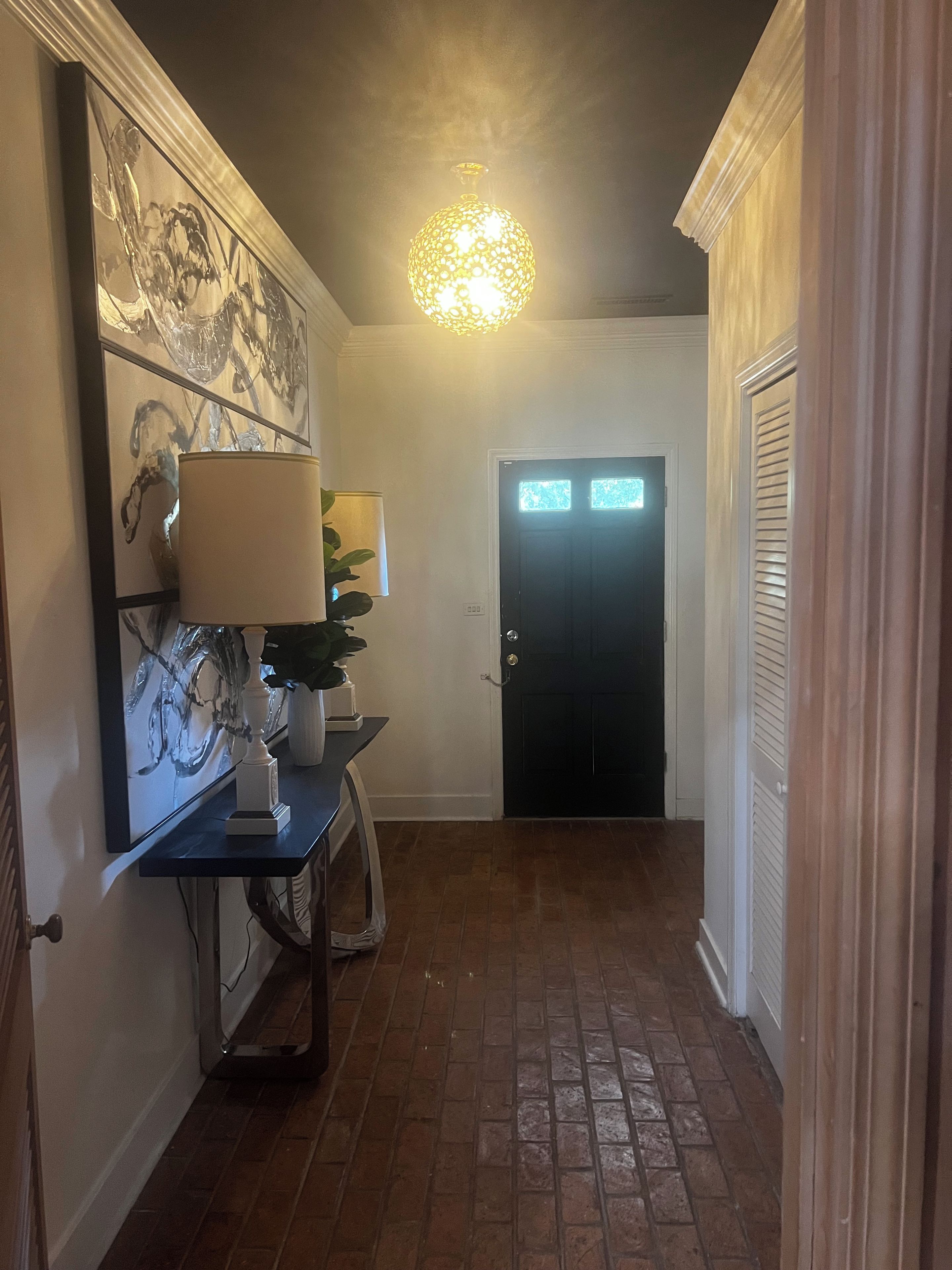 A hallway with a black door, a light fixture, and a framed abstract painting on the wall.