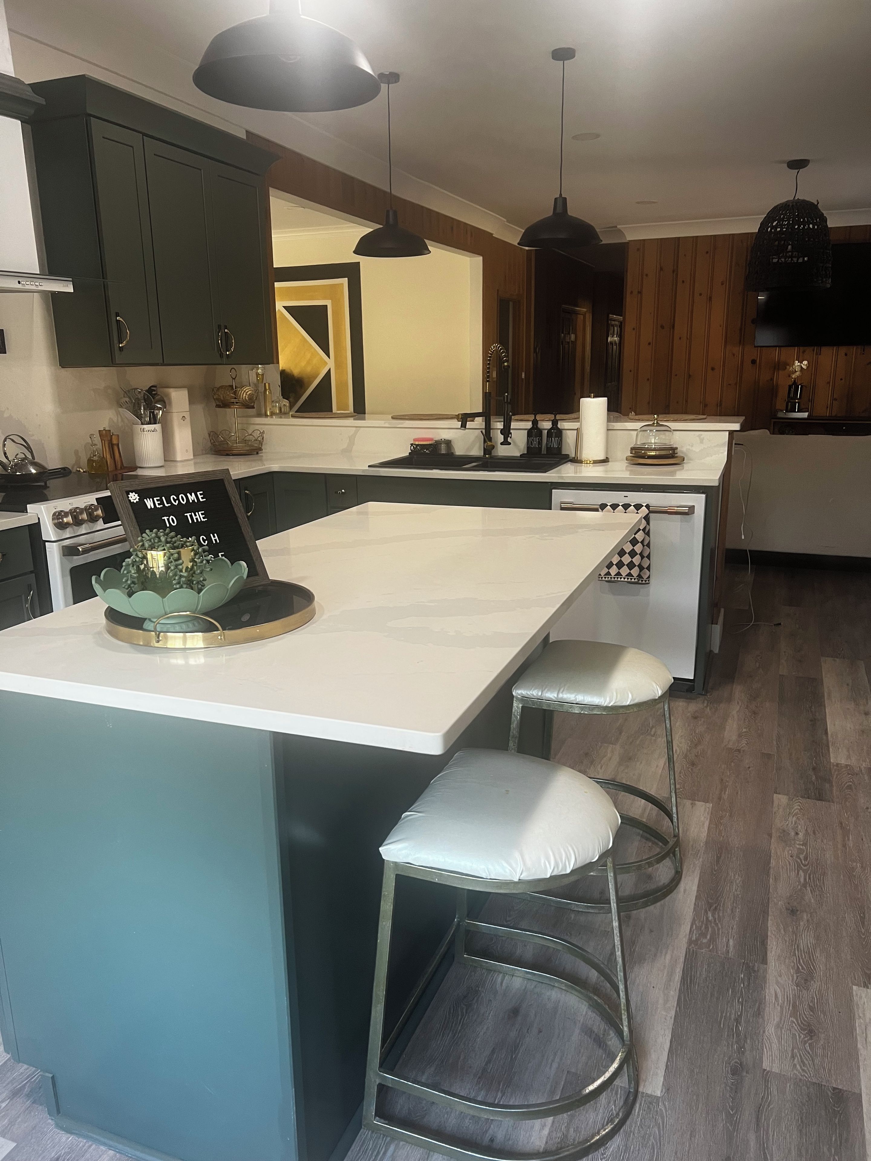 A modern kitchen with dark green cabinets, a white countertop, and a central island with bar stools.