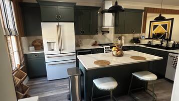 Una cocina moderna con armarios verde oscuro, una isla blanca con taburetes y un bote de basura de acero inoxidable.