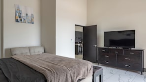 Un dormitorio moderno con una cama, un televisor sobre una cómoda y un cuadro de un paisaje urbano en la pared.
