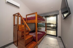 Een stapelbed met een houten trap, een flatscreen televisie en uitzicht op een waterpartij door een groot raam.