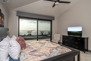 A bedroom with a large bed, a television, and a view of the sea through a sliding glass door. - New Listing • Casa Hermosa Vista • 5BR Private Villa • Ocean View (Playas del Coco)