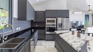 Une cuisine moderne dotée d’un grand îlot central, d’appareils électroménagers en acier inoxydable et offrant une vue sur l’extérieur.