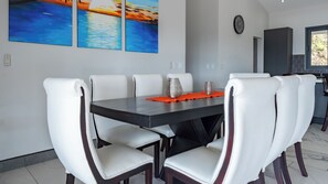 Een eetruimte met een rechthoekige tafel, zes witte stoelen en een groot schilderij erboven.