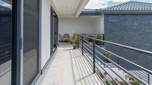 Ein Balkon mit Metallgeländer, Blumentöpfen und Blick auf ein Gebäude mit einem Ziegeldach.