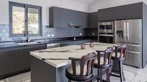 Una cocina moderna con una isla central, electrodomésticos de acero inoxidable y vistas a través de un ventanal.