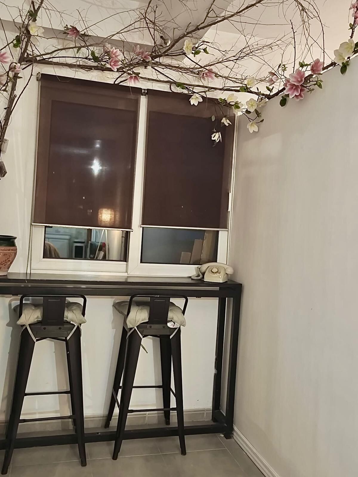 A room with a window, two bar stools, and a telephone on the windowsill.