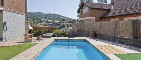 Una piscina rectangular con muelle de madera y escalera, rodeada por un cerco de madera y un césped.