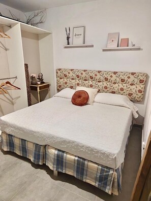 A bedroom with a bed, a wardrobe, a bedside table, and a shelf with decorative items.
