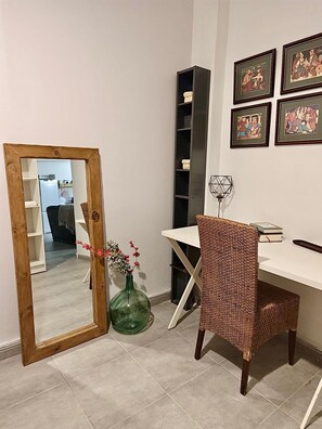 A room with a desk, chair, mirror, and framed artwork on the wall.