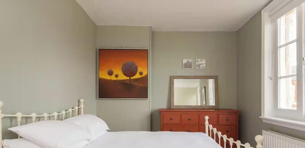 Um quarto com uma cama, cômoda, espelho e um quadro na parede.