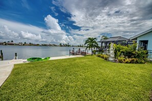 A waterfront property with a grassy lawn, a dock, and a house with a covered porch. - Villa Fun In The Sun, Lakefront Oasis with Heated Pool & Private Dock........ (Cape Coral)