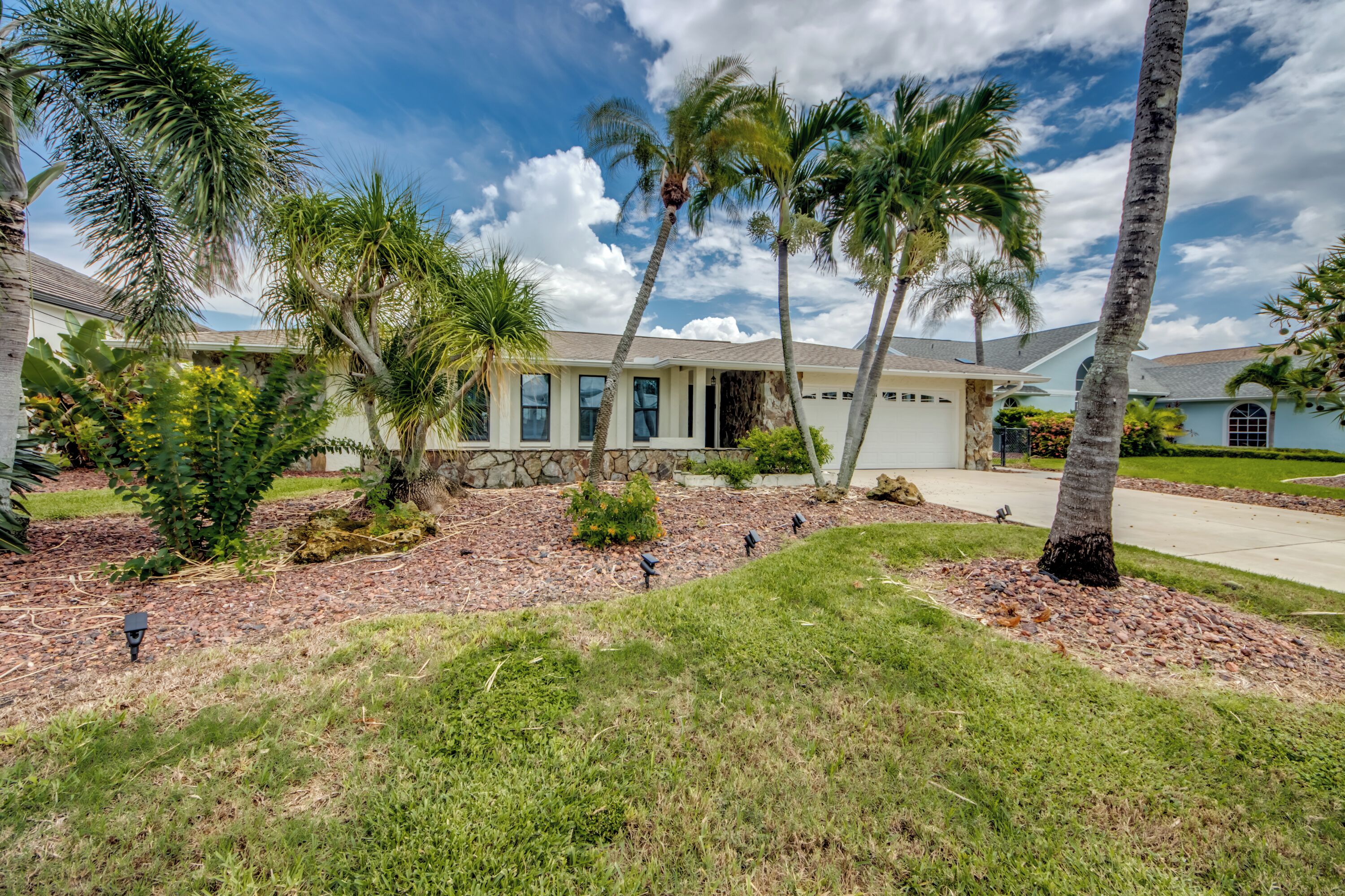 A residential property with a stone facade, a covered porch, and a well-maintained lawn with palm trees.