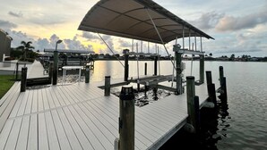 En træbrygge der strækker sig ud i roligt vand, med en overdækket siddeplads og en klar himmel.