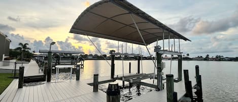 Un muelle de madera que se adentra en aguas tranquilas, con un área de estar cubierta y cielo despejado.
