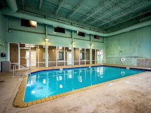 Una piscina interior con agua cristalina, borde de azulejos y una escalera de metal.