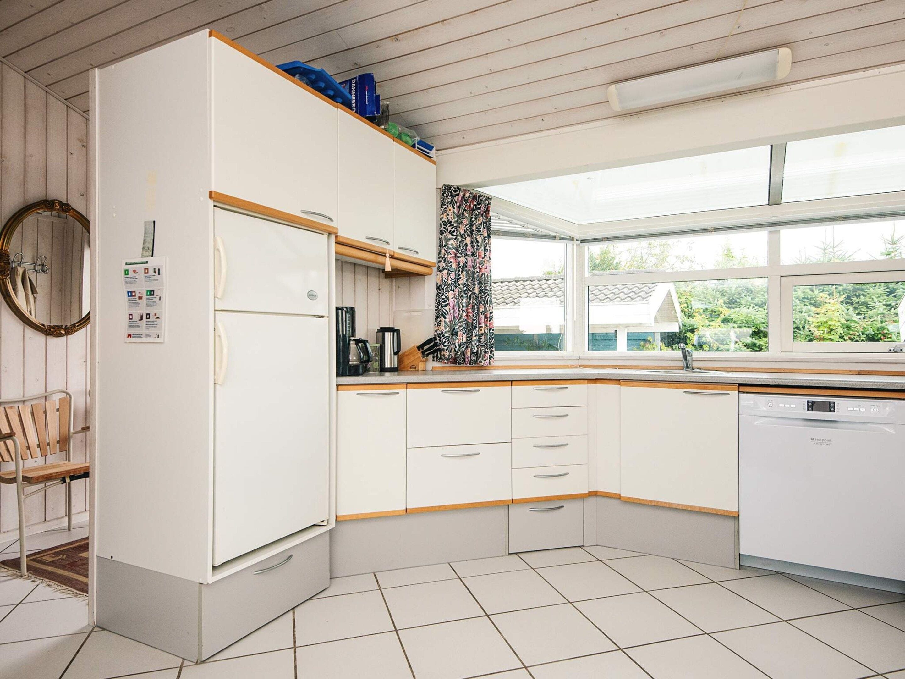 A kitchen with white cabinets, a dishwasher, and a window with a view of greenery.