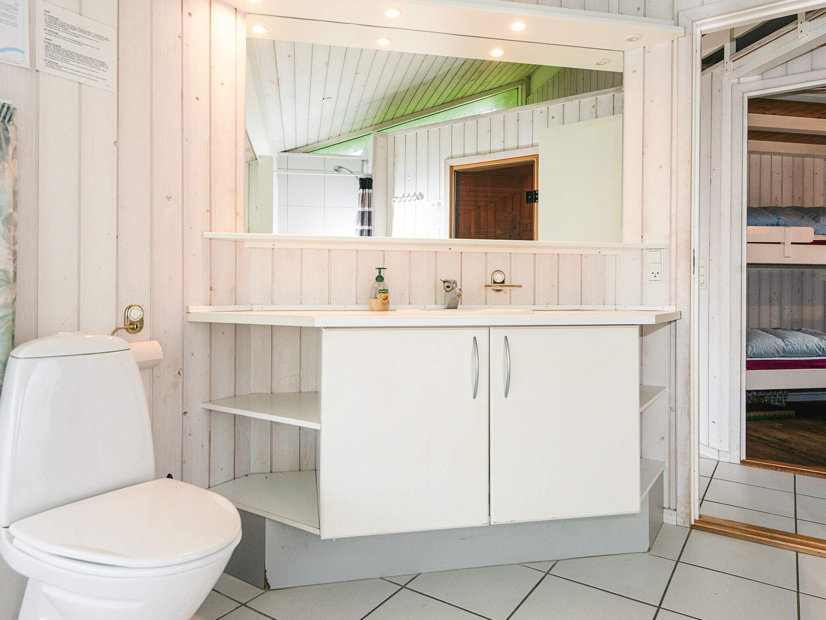 A bathroom with a toilet, a sink, a mirror, and a cabinet.