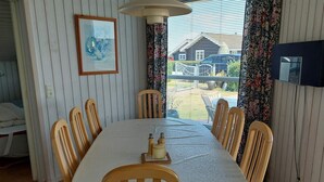A dining area with a table set for six, wooden chairs, a chandelier, a framed picture on the wall, and a view of a house through the window. - 4 Star Holiday Home in Hejls (Hejls)