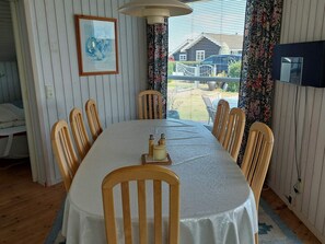 A dining area with a table set for six, wooden chairs, a chandelier, a framed picture on the wall, and a view of a house through the window. - 4 Star Holiday Home in Hejls (Hejls)