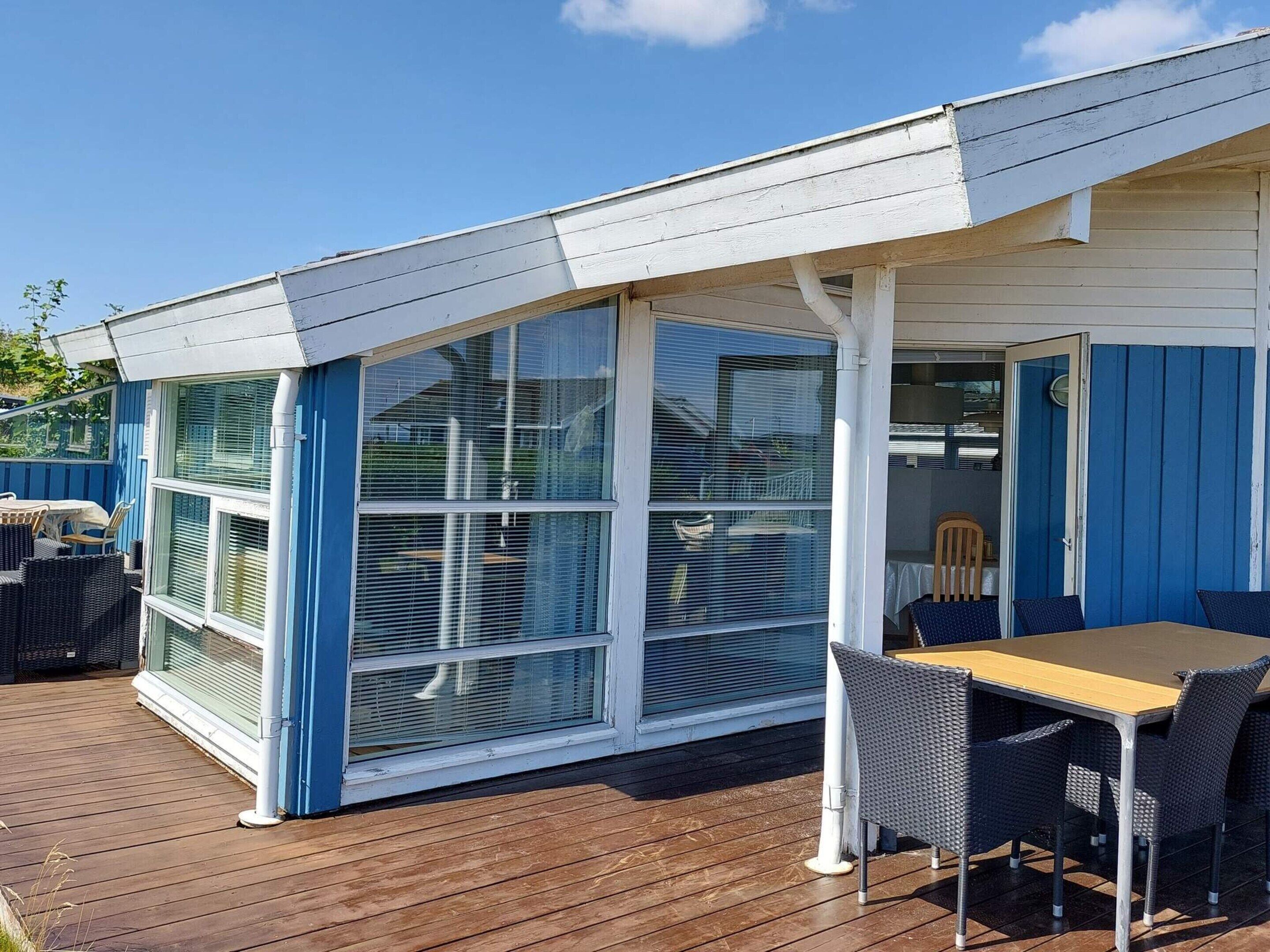 Un espace extérieur aménagé, abrité et doté d’une table et de chaises, d’une terrasse en bois et d’un bâtiment avec de grandes fenêtres.