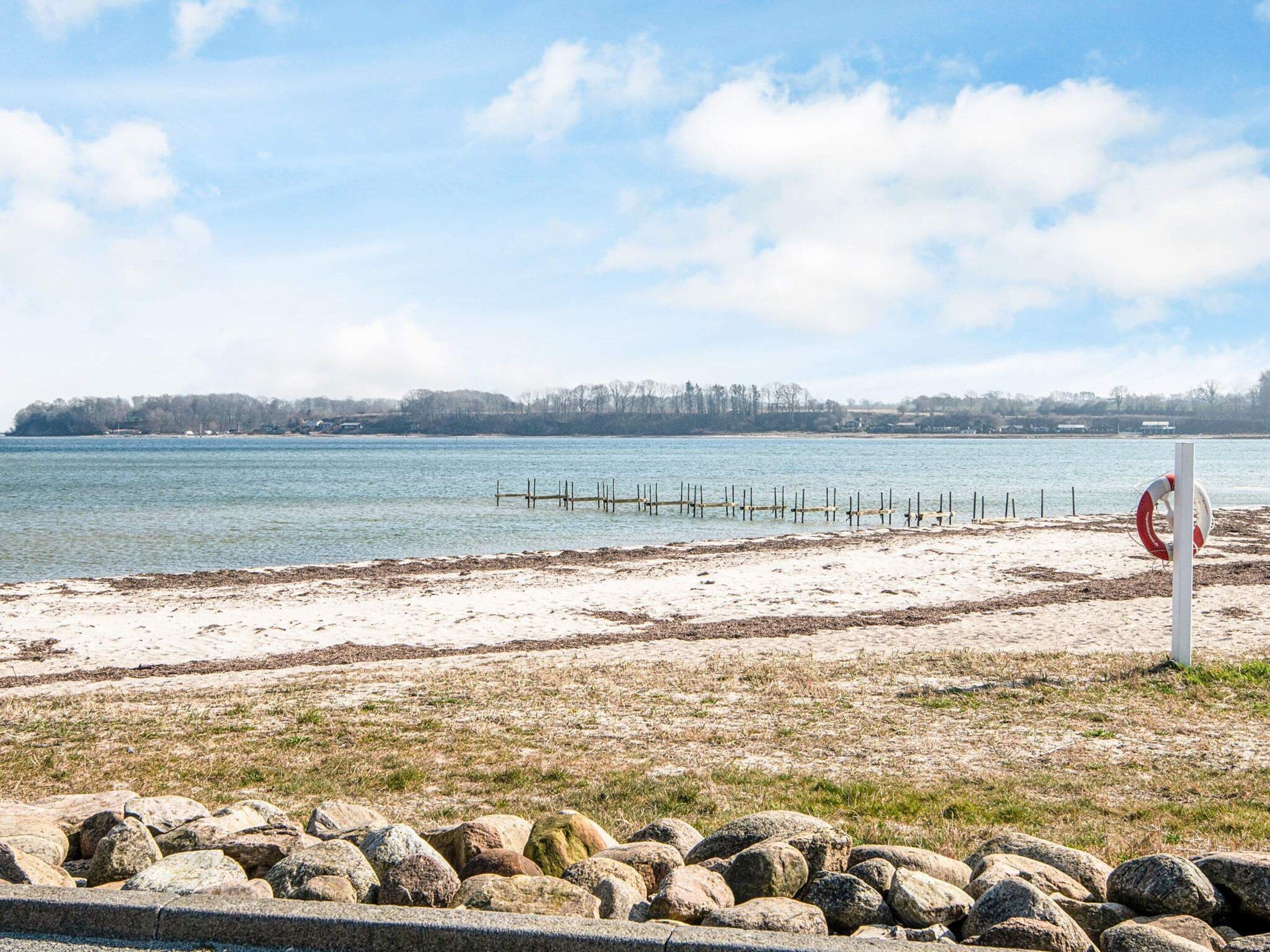 Een strand met een drijver, een houten steiger en een rotsachtige kustlijn.