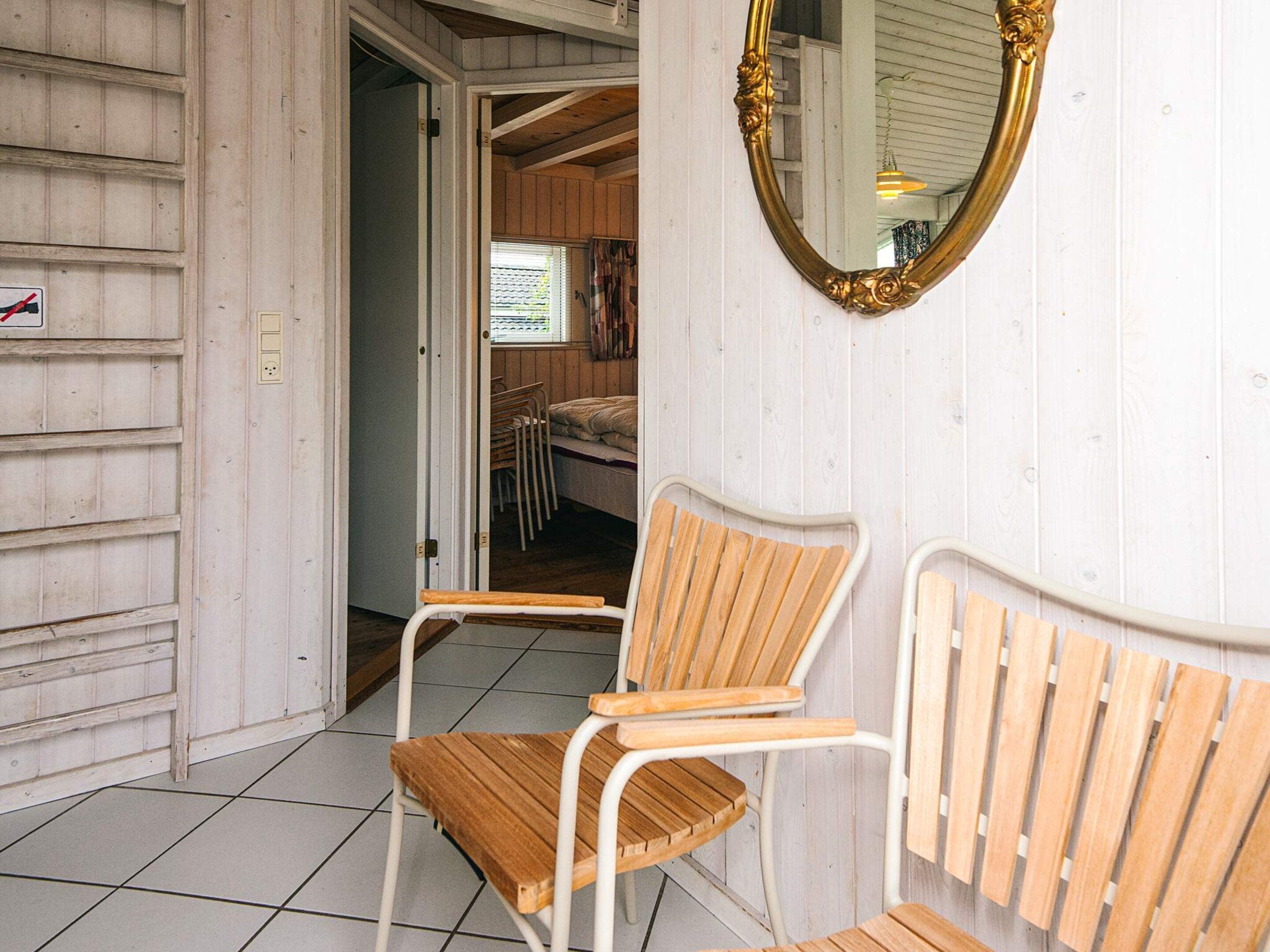 Una habitación con una silla de madera, una pared blanca y un espejo grande.