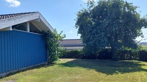 A blue building with a sloped roof, a grassy yard, and a large tree. - 4 Star Holiday Home in Hejls (Hejls)