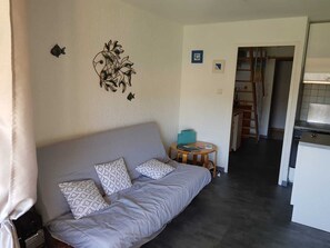 Ein Wohnzimmer mit einer Couch, Kissen, einem kleinen runden Tisch und einer Küche im Hintergrund.