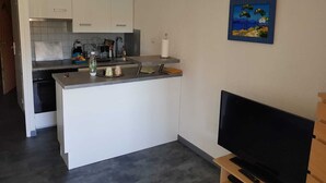 Cocina compacta con una isla central, lavavajillas integrado y un televisor de pantalla plana sobre un pedestal.