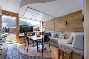Ein modernes Wohnzimmer mit großem Fernseher, Holzboden, einer Couch und einem Essbereich mit Stühlen.