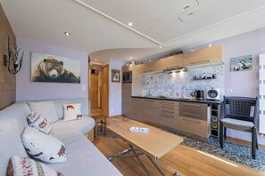 Ein modernes Wohnzimmer mit Sofa, Couchtisch, Küchenzeile mit Holzschränken und einem Esstisch.