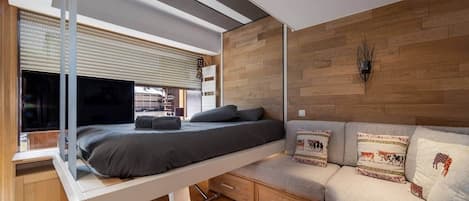 Un dormitorio moderno con cama, sofá, televisor y pared de madera.