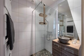 Ein modernes Badezimmer mit Duschkabine aus Glas, einem Holzwaschtisch mit Steinbecken und einem großen Spiegel, der den Raum reflektiert.