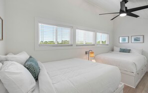 Ein Schlafzimmer mit zwei Betten, weißer Bettwäsche, einem Deckenventilator und einem Fenster mit Jalousien.