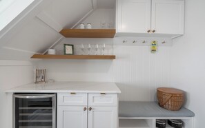 Eine Küchenzeile mit Einbauofen, kleinem Kühlschrank und einem Holzregal über der Arbeitsplatte.