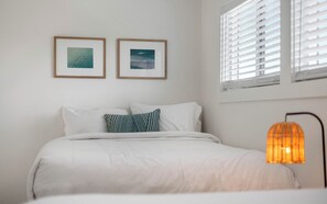 A bedroom with a bed, two framed pictures on the wall, and a window with blinds. - Salt Haus 30A: Pet Friendly Gulf View Loft (Santa Rosa Beach)
