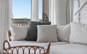 Ein Balkon mit einem Holzstuhl, einer gepolsterten Couch mit Kissen und Blick auf den Himmel und ein Gebäude.