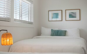 Ein Schlafzimmer mit einem Bett, zwei Kissen, einem Wandbild und einem Fenster mit Jalousien.
