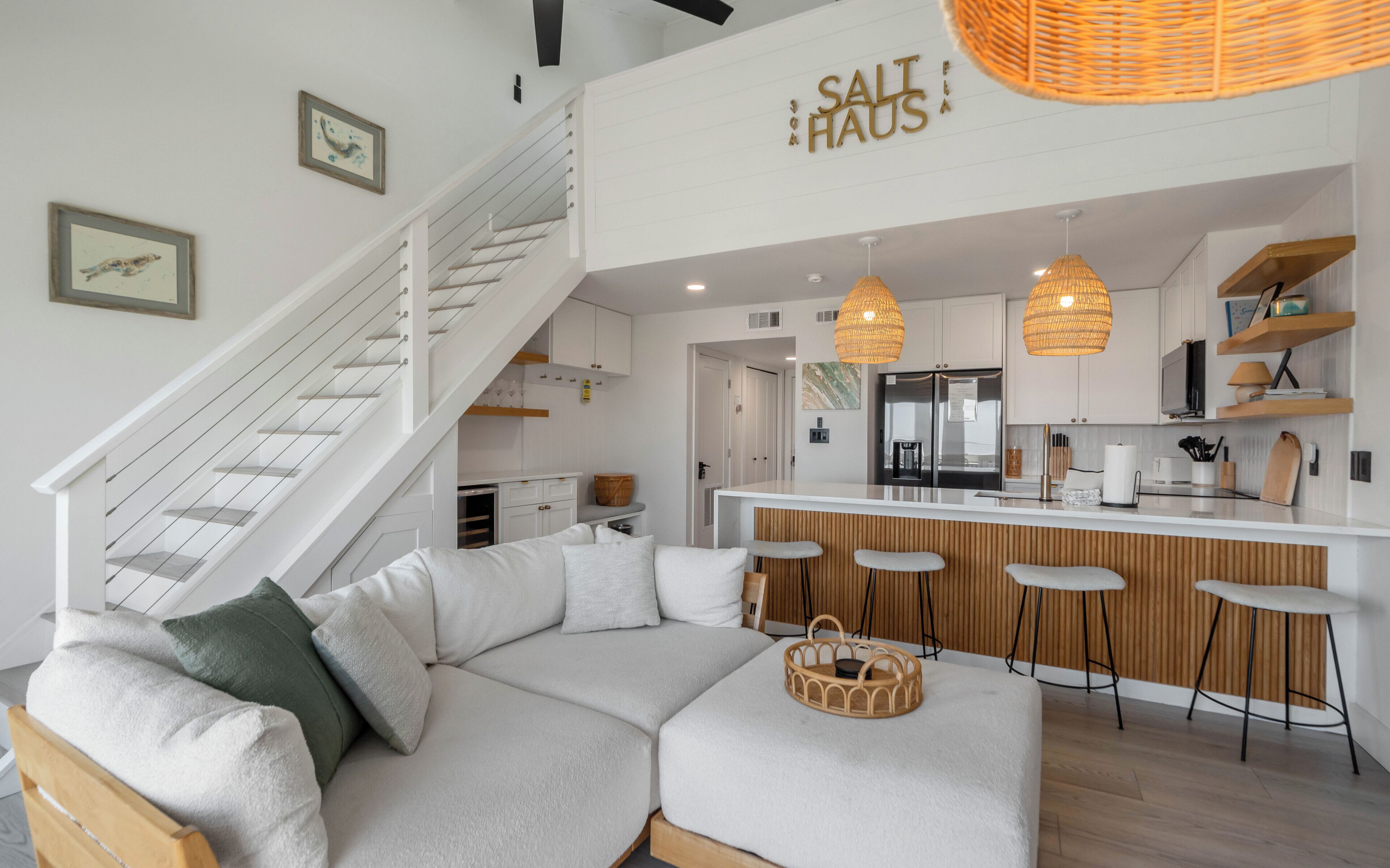 Una cocina moderna con una isla central, taburetes de bar y una escalera que sube a un nivel superior.