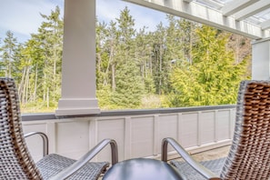 A covered outdoor seating area with wicker chairs and a view of a forest. - Family & Dog friendly Nedonna Beach Home, Hot Tub, BBQ, Short Walk to the Beach (Rockaway Beach)